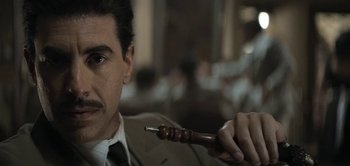 Movie still from “The Spy” (2019), directed by Gideon Raff – A man in a suit and tie holding an object in his hand; Close Up shot, High angle