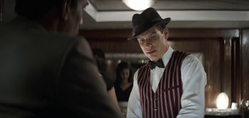 Movie still from “The Spy” (2019), directed by Gideon Raff – A man wearing a hat and a striped vest talking to another man; Medium shot, Over the shoulder angle