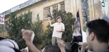 Movie still from “The Spy” (2019), directed by Gideon Raff – A man holding a gun in a crowd of people; Wide shot, Low angle