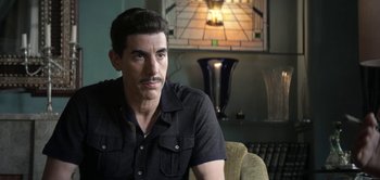 Movie still from “The Spy” (2019), directed by Gideon Raff – A person sitting on a couch in a living room; Close Up shot, Over the shoulder angle