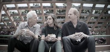 Movie still from “The Spy” (2019), directed by Gideon Raff – A group of people sitting next to each other holding sandwiches; Medium shot, Over the shoulder angle