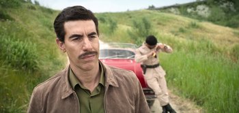 Movie still from “The Spy” (2019), directed by Gideon Raff – A man standing next to a red car on a dirt road; Close Up shot, Over the shoulder angle