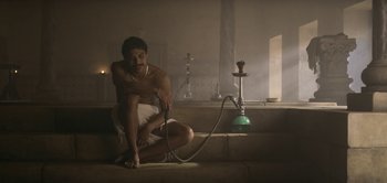 Movie still from “The Spy” (2019), directed by Gideon Raff – A man sitting on a step with a hookah pipe; Wide shot, Low angle