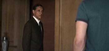 Movie still from “The Spy” (2019), directed by Gideon Raff – A man wearing a suit and tie standing in front of a door; Medium shot, Over the shoulder angle