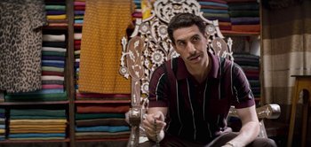 Movie still from “The Spy” (2019), directed by Gideon Raff – A man sitting on a chair in a room; Medium shot, Over the shoulder angle