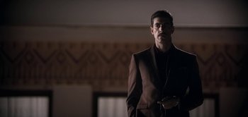 Movie still from “The Spy” (2019), directed by Gideon Raff – A man wearing a suit and tie standing in a room; Medium shot, Low angle