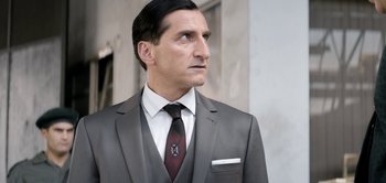 Movie still from “The Spy” (2019), directed by Gideon Raff – A man in a suit and tie standing outside; Close Up shot, Low angle