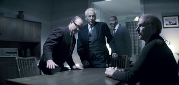 Movie still from “The Spy” (2019), directed by Gideon Raff – A group of men standing around a wooden table; Medium shot, Over the shoulder angle
