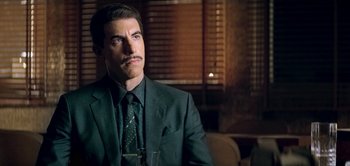Movie still from “The Spy” (2019), directed by Gideon Raff – A man wearing a suit and tie sitting in front of a window; Close Up shot, Over the shoulder angle