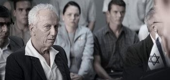 Movie still from “The Spy” (2019), directed by Gideon Raff – An old man and a group of people sitting in front of him; Close Up shot, Over the shoulder angle