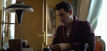 Movie still from “The Spy” (2019), directed by Gideon Raff – A man sitting at a table writing on a piece of paper; Medium shot, Low angle