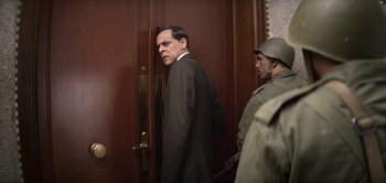 Movie still from “The Spy” (2019), directed by Gideon Raff – A man standing in front of a wooden door; Medium shot, Over the shoulder angle