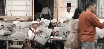 Movie still from “The Spy” (2019), directed by Gideon Raff – A group of men sitting at a table reading newspapers; Wide shot, High angle