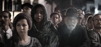 Movie still from “The Spy” (2019), directed by Gideon Raff – A group of people standing around each other in the dark; Medium shot, Over the shoulder angle