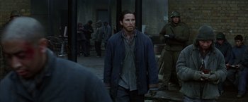 Movie still from “Batman Begins” (2005), directed by Christopher Nolan – A man standing on a street in front of a group of people; Medium shot, Over the shoulder angle