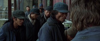 Movie still from “Batman Begins” (2005), directed by Christopher Nolan – A group of people in a line wearing hats; Medium shot, Over the shoulder angle