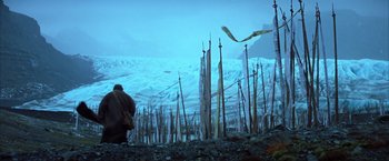 Movie still from “Batman Begins” (2005), directed by Christopher Nolan – A man standing on top of a hill next to trees; Extreme Wide shot, Low angle