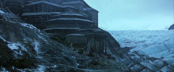 Movie still from “Batman Begins” (2005), directed by Christopher Nolan – A building on top of a mountain in the rain; Extreme Wide shot, High angle