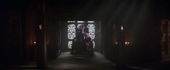 Movie still from “Batman Begins” (2005), directed by Christopher Nolan – A person sitting in front of an open door; Wide shot, High angle