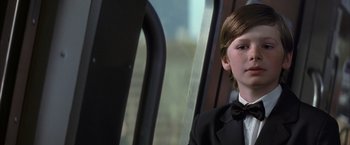 Movie still from “Batman Begins” (2005), directed by Christopher Nolan – A boy in a tuxedo sitting on a bus; Close Up shot, Low angle