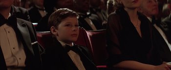 Movie still from “Batman Begins” (2005), directed by Christopher Nolan – A boy in a tuxedo sitting in front of an audience; Close Up shot, High angle