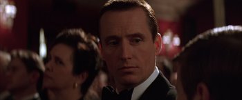 Movie still from “Batman Begins” (2005), directed by Christopher Nolan – A man in a suit and bow tie looking to his left; Close Up shot, Low angle