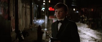 Movie still from “Batman Begins” (2005), directed by Christopher Nolan – A boy in a suit and bow tie standing in the dark; Medium shot, Over the shoulder angle