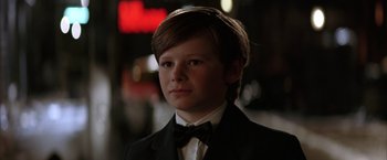 Movie still from “Batman Begins” (2005), directed by Christopher Nolan – A young boy in a suit and bow tie; Close Up shot, Over the shoulder angle