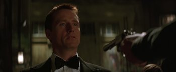 Movie still from “Batman Begins” (2005), directed by Christopher Nolan – A person wearing a suit holding a gun; Close Up shot, Low angle