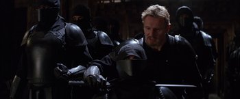 Movie still from “Batman Begins” (2005), directed by Christopher Nolan – A group of men in black suits and helmets; Medium shot, Over the shoulder angle