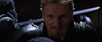 Movie still from “Batman Begins” (2005), directed by Christopher Nolan – A person with a beard looking at the camera; Close Up shot, Low angle