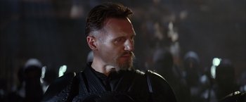 Movie still from “Batman Begins” (2005), directed by Christopher Nolan – A person with a beard wearing a suit; Close Up shot, Over the shoulder angle