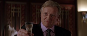 Movie still from “Batman Begins” (2005), directed by Christopher Nolan – An older man in a suit holding a wine glass; Close Up shot, Low angle