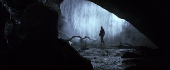 Movie still from “Batman Begins” (2005), directed by Christopher Nolan – A man standing in front of a waterfall; Wide shot, Over the shoulder angle