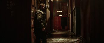 Movie still from “Batman Begins” (2005), directed by Christopher Nolan – A man standing in a dark hallway in the dark; Wide shot, Low angle