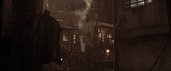 Movie still from “Batman Begins” (2005), directed by Christopher Nolan – A person standing in the rain under a cloudy sky; Wide shot, Low angle
