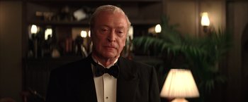 Movie still from “Batman Begins” (2005), directed by Christopher Nolan – An older man wearing a tuxedo and a bow tie; Close Up shot, Over the shoulder angle