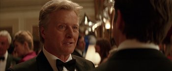 Movie still from “Batman Begins” (2005), directed by Christopher Nolan – An older man in a tuxedo is talking to a younger man; Close Up shot, Over the shoulder angle