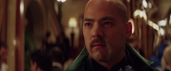Movie still from “Batman Begins” (2005), directed by Christopher Nolan – A man with a mustache and a goatee looking at the camera; Close Up shot, Low angle