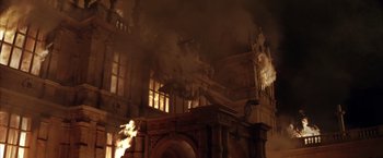 Movie still from “Batman Begins” (2005), directed by Christopher Nolan – A fire is burning in a building with a clock; Extreme Wide shot, Low angle
