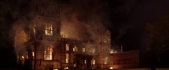 Movie still from “Batman Begins” (2005), directed by Christopher Nolan – A large building that is on fire at night; Extreme Wide shot, Low angle