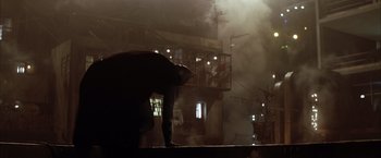 Movie still from “Batman Begins” (2005), directed by Christopher Nolan – A man standing on top of a building in the dark; Wide shot, Low angle