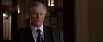 Movie still from “Batman Begins” (2005), directed by Christopher Nolan – An older man wearing a suit and tie; Close Up shot, Low angle