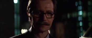 Movie still from “Batman Begins” (2005), directed by Christopher Nolan – A person wearing glasses and a suit; Close Up shot, Low angle