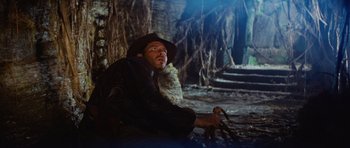 Movie still from “Raiders of the Lost Ark” (1981), directed by Steven Spielberg – A man sitting on the ground in a forest; Wide shot, Low angle