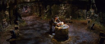 Movie still from “Raiders of the Lost Ark” (1981), directed by Steven Spielberg – A man in a hat and a brown jacket standing next to a barrel; Wide shot, High angle