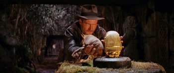 Movie still from “Raiders of the Lost Ark” (1981), directed by Steven Spielberg – A man in a hat and gloves holding a jar; Medium shot, Low angle