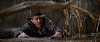 Movie still from “Raiders of the Lost Ark” (1981), directed by Steven Spielberg – A man laying on the ground wearing a hat; Medium shot, Low angle