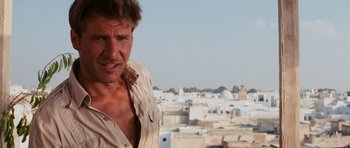 Movie still from “Raiders of the Lost Ark” (1981), directed by Steven Spielberg – A man standing on top of a building near a bunch of buildings; Close Up shot, Low angle