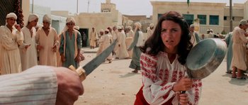 Movie still from “Raiders of the Lost Ark” (1981), directed by Steven Spielberg – A woman in a red and white dress holding a knife; Medium shot, Over the shoulder angle